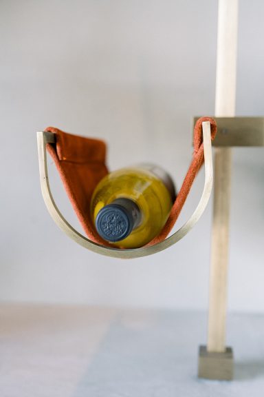 Cradled in brass and leather Close-up of a wine bottle cradled in soft rust-toned leather with custom brass wall-mounted supports.